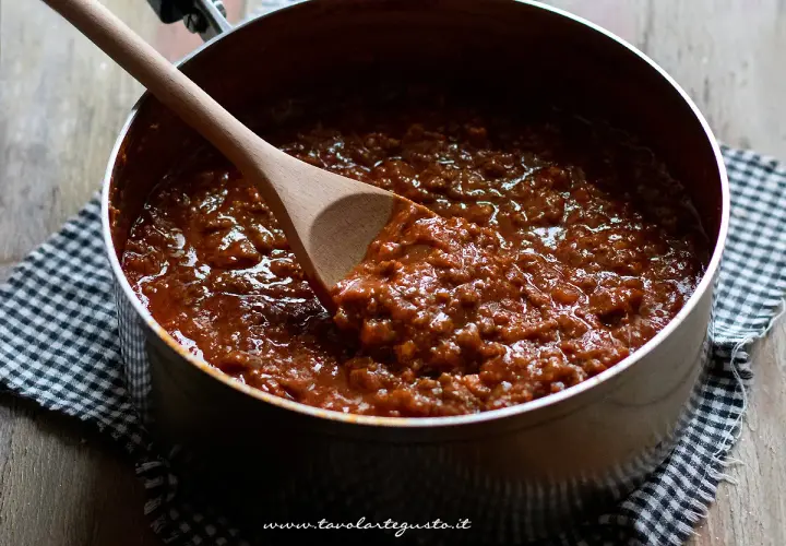 Un pentolino pieno di ragù alla bolognese, pronto per condire la pasta. Un cucchiaio di legno affonda nella salsa densa e profumata.