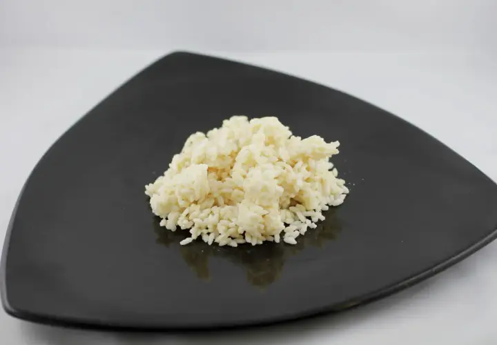 Un mucchietto di riso bianco cotto su un piatto nero, pronto per essere gustato. Ecco come cuocere il riso per un risultato perfetto.