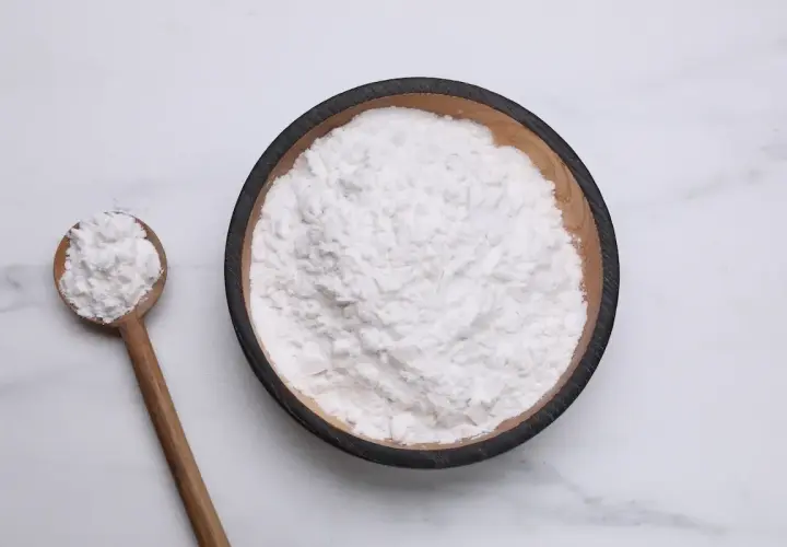 Una ciotola di amido di riso per dolci, con un cucchiaio di legno pieno dello stesso ingrediente soffice.