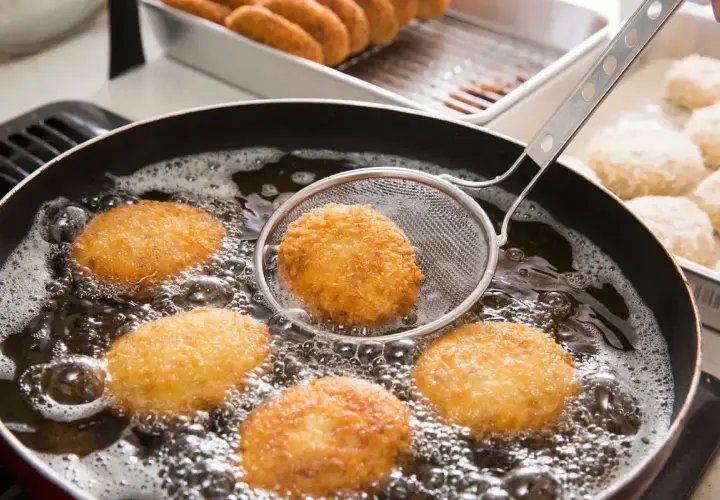 Crocchette dorate che sfrigolano nell'olio bollente, un perfetto esempio di come friggere per ottenere una croccantezza irresistibile.