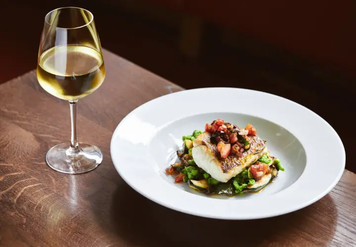 Piatto di pesce con verdure e un bicchiere di vino bianco, perfetti abbinamenti per una ribolla gialla.
