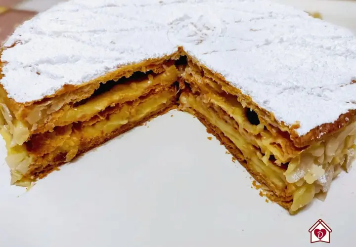 Una deliziosa torta millefoglie con strati di pasta sfoglia croccante e crema pasticcera, cosparsa di zucchero a velo e mandorle.