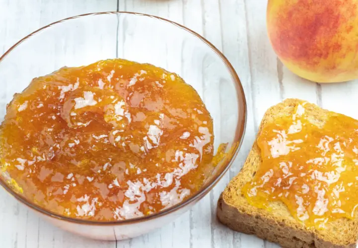Una ciotola di marmellata di pesche fatta in casa e una fetta biscottata imburrata con la stessa deliziosa marmellata.