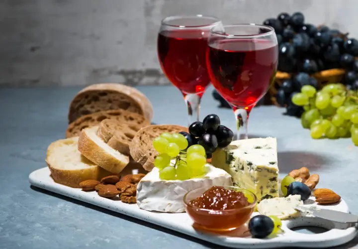 Due calici di rosato vino accompagnano un tagliere con pane, formaggi, uva e frutta secca.