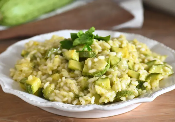 Un cremoso risotto con zucchine, guarnito con prezzemolo fresco, servito in un piatto bianco.