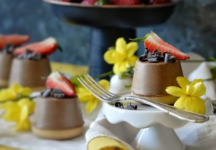 Mini cheesecake al cioccolato con fragola e riccioli di cioccolato, decorati con fiori gialli.