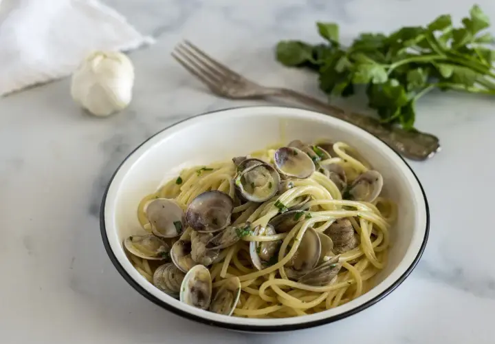 Un piatto invitante di spaghetti alle vongole, con aglio e prezzemolo freschi sullo sfondo.