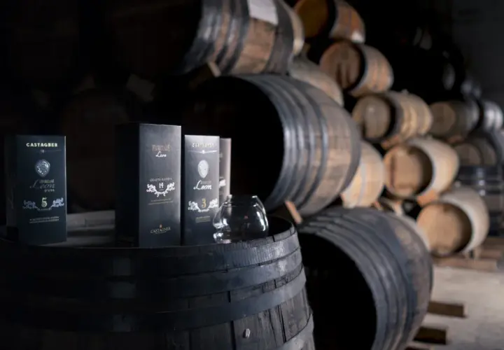 Bottiglie di grappa Castagner su botti di legno. Il significato di grappa barricata è legato all'affinamento in botte, che dona colore e aromi complessi.