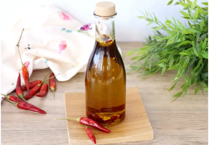 Una bottiglia di olio al peperoncino, con peperoncini rossi secchi sparsi intorno e un tocco di verde sullo sfondo.
