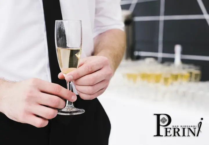 Un bicchiere di prosecco vino dorato, tenuto da mani eleganti, con una piramide di calici sullo sfondo.