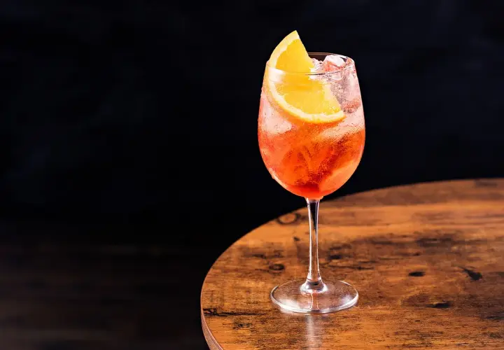 Un bicchiere di spritz Italia, rinfrescante e colorato, con una fetta d'arancia, su un tavolo di legno.