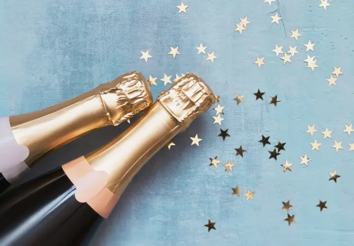 Due bottiglie di spumante dorato su sfondo blu con stelle dorate. Una celebrazione che fa pensare alla differenza tra prosecco e spumante.