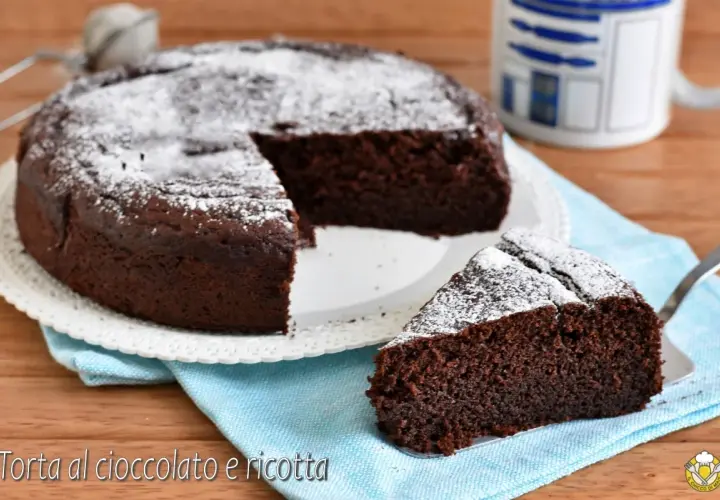 Una deliziosa torta al cioccolato e ricotta, cosparsa di zucchero a velo, con una fetta servita su un tovagliolo azzurro.