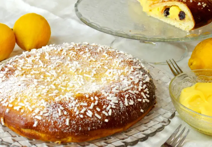 Una deliziosa polacca aversana, cosparsa di zucchero a velo e confettini, accanto a limoni freschi e crema pasticcera.