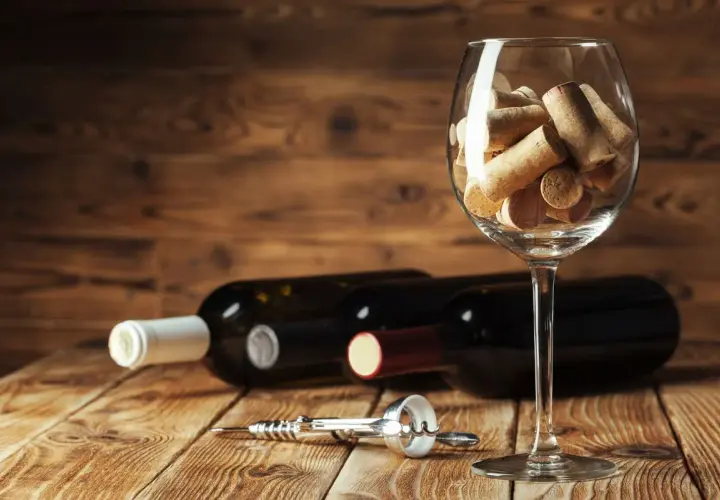 Tappi di sughero in un calice, bottiglie di vino e cavatappi sul tavolo. Un promemoria visivo su come chiudere una bottiglia di vino.