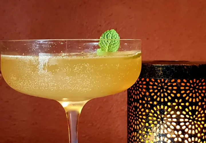 Rinfrescante cocktail con rum e menta, guarnito con una fogliolina verde, accanto a una lanterna decorativa che emana luce calda.