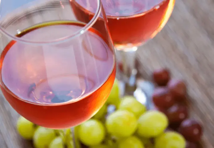 Due calici di vino rosato, frutto della vinificazione in rosato, con grappoli d'uva verde e rossa sullo sfondo.