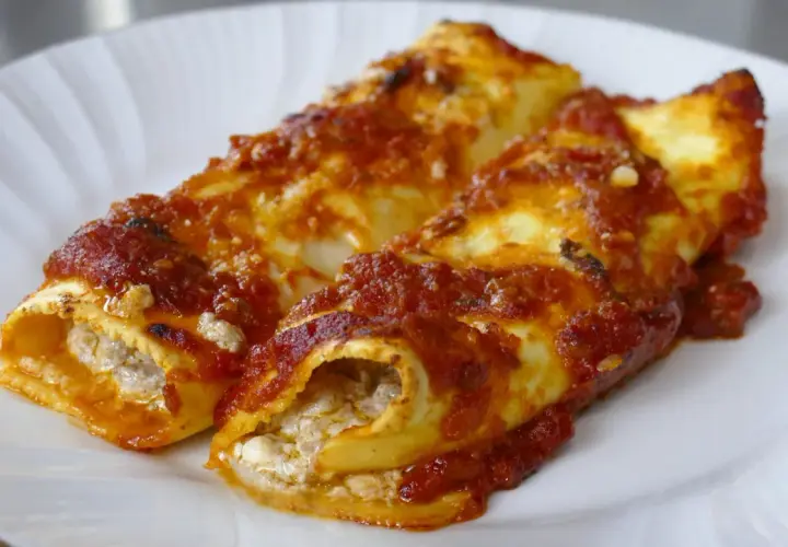 Due cannelloni ripieni, ricoperti di sugo rosso e formaggio, pronti per essere gustati.