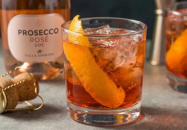 Un Negroni Sbagliato con Prosecco Rosé, guarnito con scorza d'arancia, ghiaccio e una bottiglia di Prosecco Villa Sparina sullo sfondo.