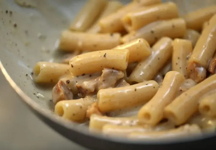 Primo piatto di pasta con guanciale croccante e crema al pecorino romano, un classico saporito.