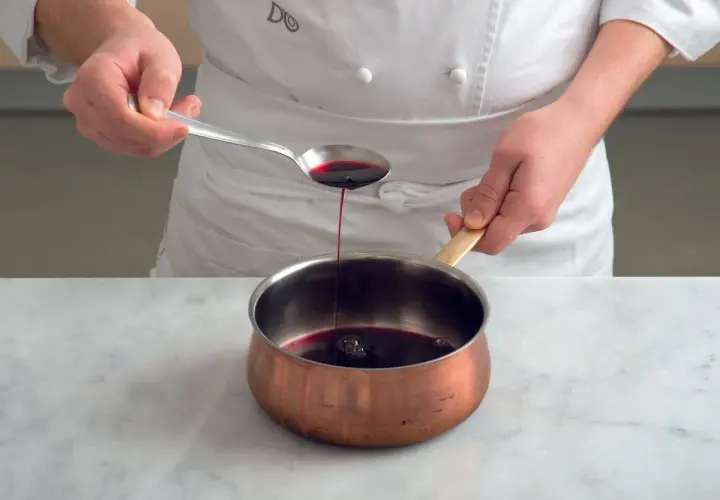 Chef versa un cucchiaio di riduzione di vino rosso in una pentola di rame.