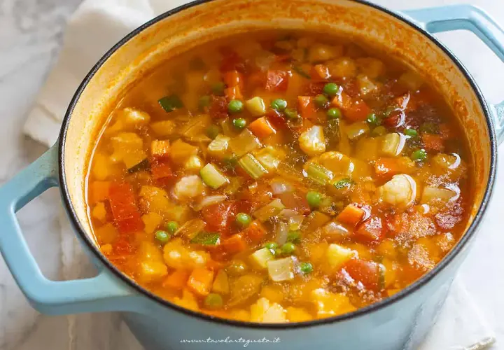 Un fumante minestrone di verdure in una pentola azzurra, ricco di carote, zucchine, piselli e cavolfiore.