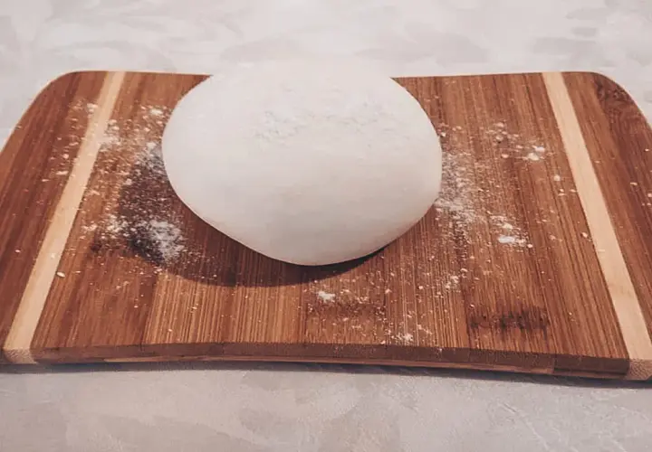 Palla di pasta di zucchero bianca su tagliere di legno, pronta per essere modellata.