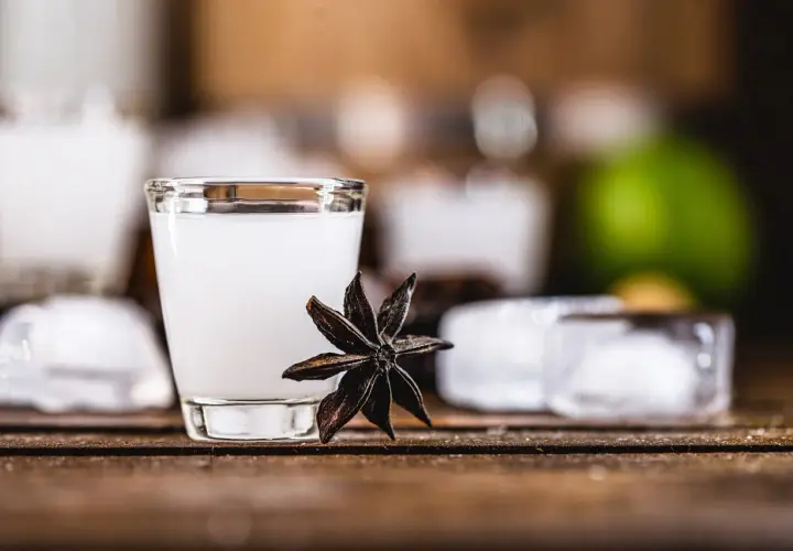 Un bicchierino di cocktail con la sambuca, guarnito con anice stellato, cubetti di ghiaccio e una fetta di lime sullo sfondo.