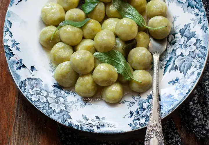 Gnocchi di zucchine soffici e profumati, guarniti con foglie di salvia fresca su un piatto decorato.