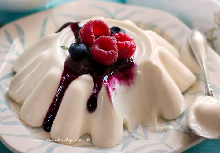 Deliziosa panna cotta con frutti di bosco e salsa ai mirtilli, servita su un piatto decorato.