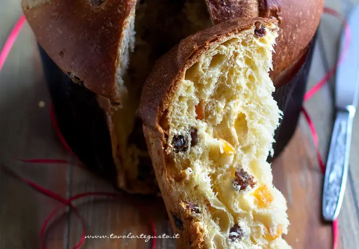 Un dolce panettone casalingo, soffice e profumato, con canditi e uvetta. Una fetta mostra la sua morbidezza e il colore dorato.