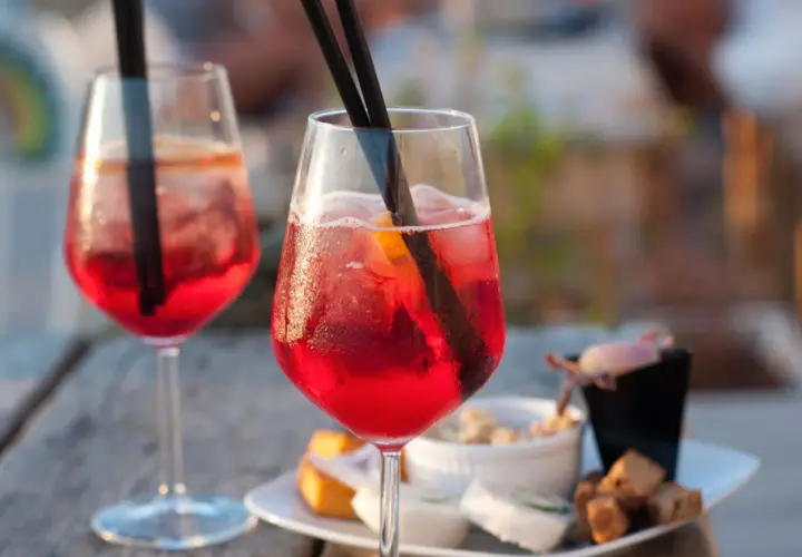Due cocktail rossi con ghiaccio e arancia, accompagnati da stuzzichini. Perfetti per un aperitivo, ecco la pirlo bianco ricetta.