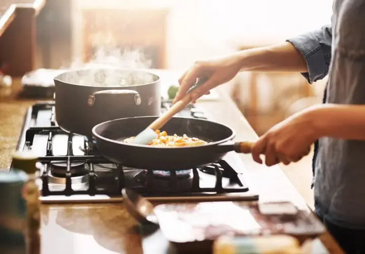 Mani che mescolano verdure in padella, mentre l'acqua bolle in pentola. Un'immagine che evoca il **macerare significato** in cucina: preparare ingredienti con cura.