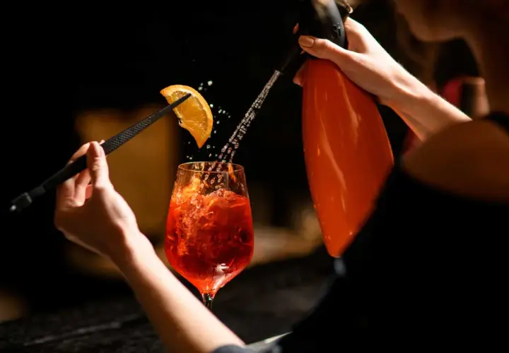 Un barista prepara un Pirlo Spritz, spruzzando acqua frizzante su una fetta d'arancia che decora il bicchiere.