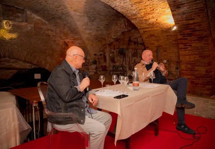 Due uomini discutono del metodo champagne in una cantina storica, con bicchieri da degustazione pronti.