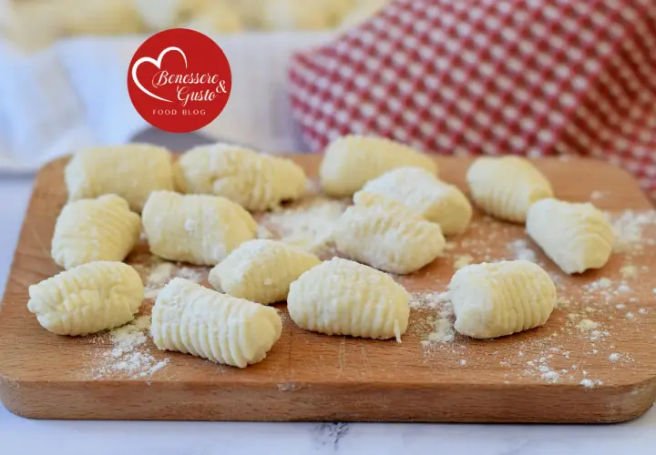 Gnocchi di ricotta freschi, pronti per essere cucinati, spolverati di farina su un tagliere di legno.