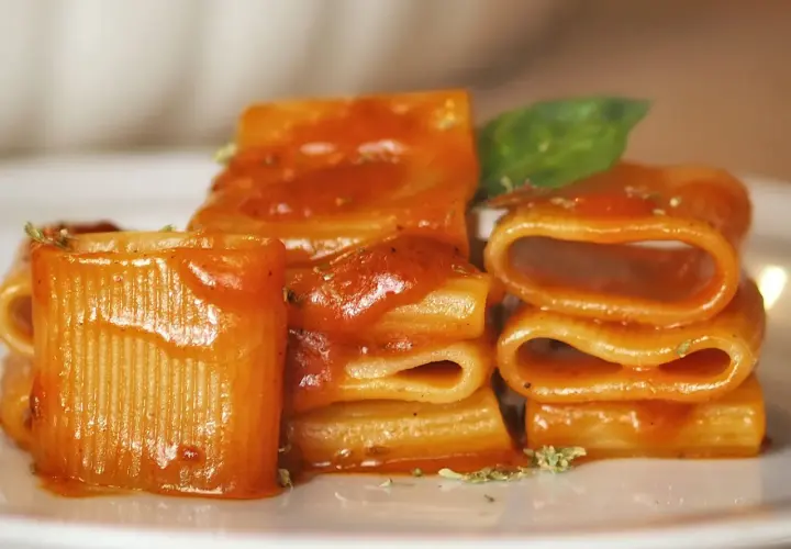 Un primo piatto invitante: paccheri conditi con un sugo rosso vivace, un classico della **pasta allo scarpariello**, guarnito con basilico fresco.