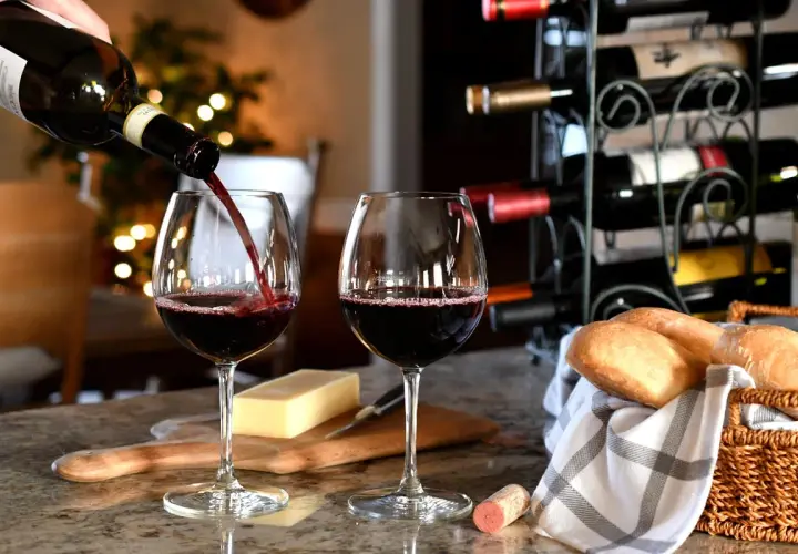 Versare vino rosso in un bicchiere, con pane e formaggio. Un promemoria su come conservare il vino rosso per gustarlo al meglio.