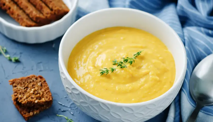 Una ciotola di cremosa salsa di ceci, guarnita con timo, accanto a fette di pane integrale e un tovagliolo blu a righe.