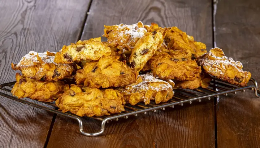 Un mucchio di croccanti biscotti alle corn flakes e uvetta, spolverati di zucchero a velo, sembrano piccole rose del deserto su una griglia.