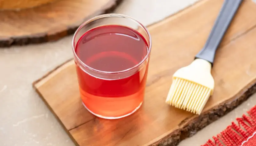 Bagna all'alchermes in un bicchiere, pronta per essere usata con un pennello da cucina su un tagliere di legno.