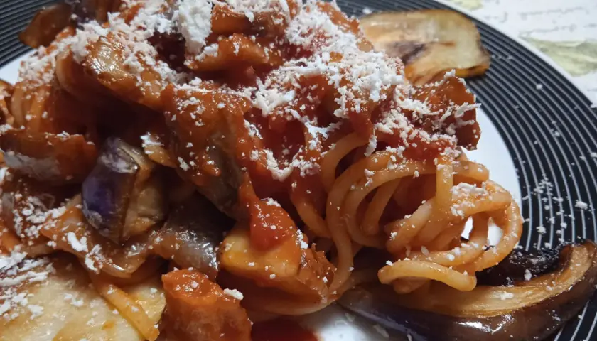 Un piatto invitante di pasta con melanzane, condita con sugo rosso e abbondante formaggio grattugiato.