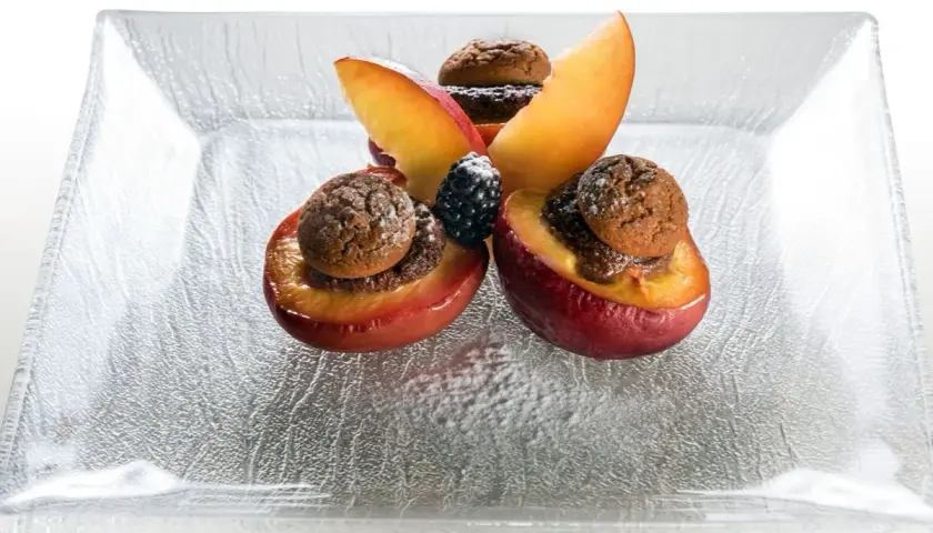 Deliziose pesche ripiene alla piemontese, guarnite con amaretti e frutti di bosco, su un piatto di vetro.