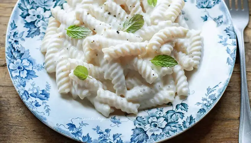 Fusilli cremosi con un sugo leggero alla ricotta, guarniti con foglie di menta fresca su un piatto decorato.