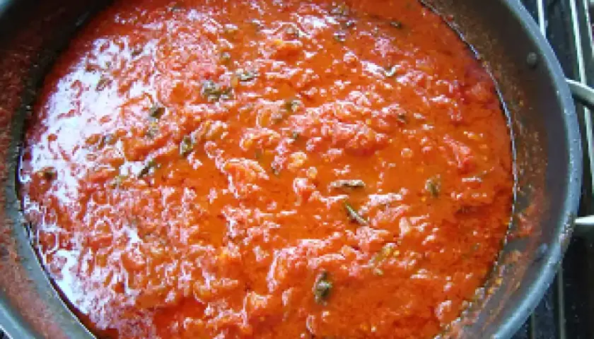 Sugo di pomodoro fresco in padella, profumato con erbe aromatiche, pronto per condire la pasta.