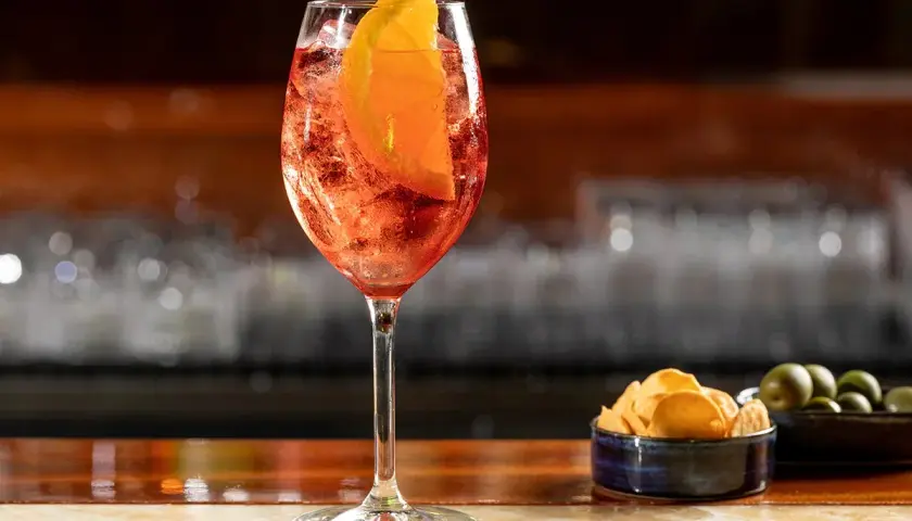 Un rinfrescante cocktail spritz, con una fetta d'arancia e ghiaccio, servito su un bancone di legno lucido.