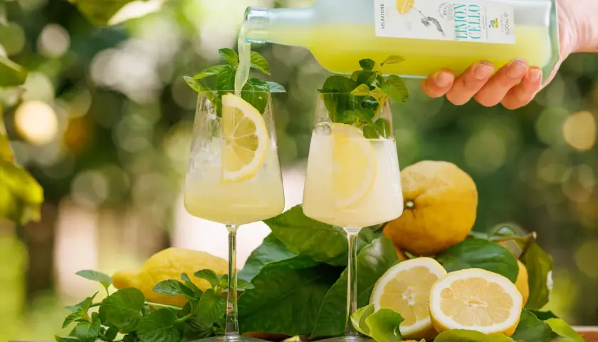 Un rinfrescante amalfi spritz viene versato in due bicchieri con limone e menta, circondati da limoni freschi e foglie verdi.