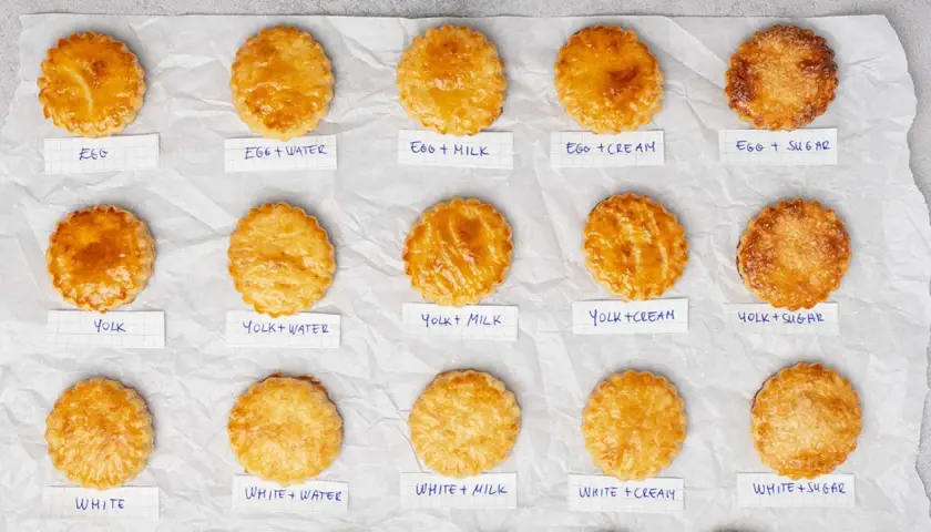 Quindici pasticcini dorati, ognuno con un'etichetta che indica il tipo di egg wash usato per ottenere la sua lucentezza.