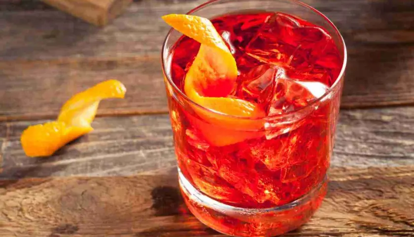 Un Negroni Sbagliato, con la sua vibrante gradazione di rosso, servito con ghiaccio e una scorza d'arancia su un tavolo di legno.