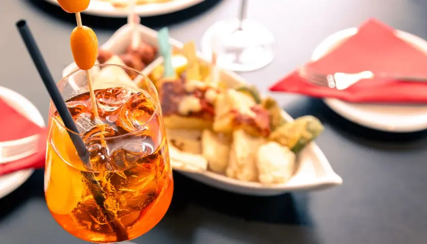 Un bicchiere di spritz aperitivo con amici, ghiaccio e arancia, accompagnato da stuzzichini.